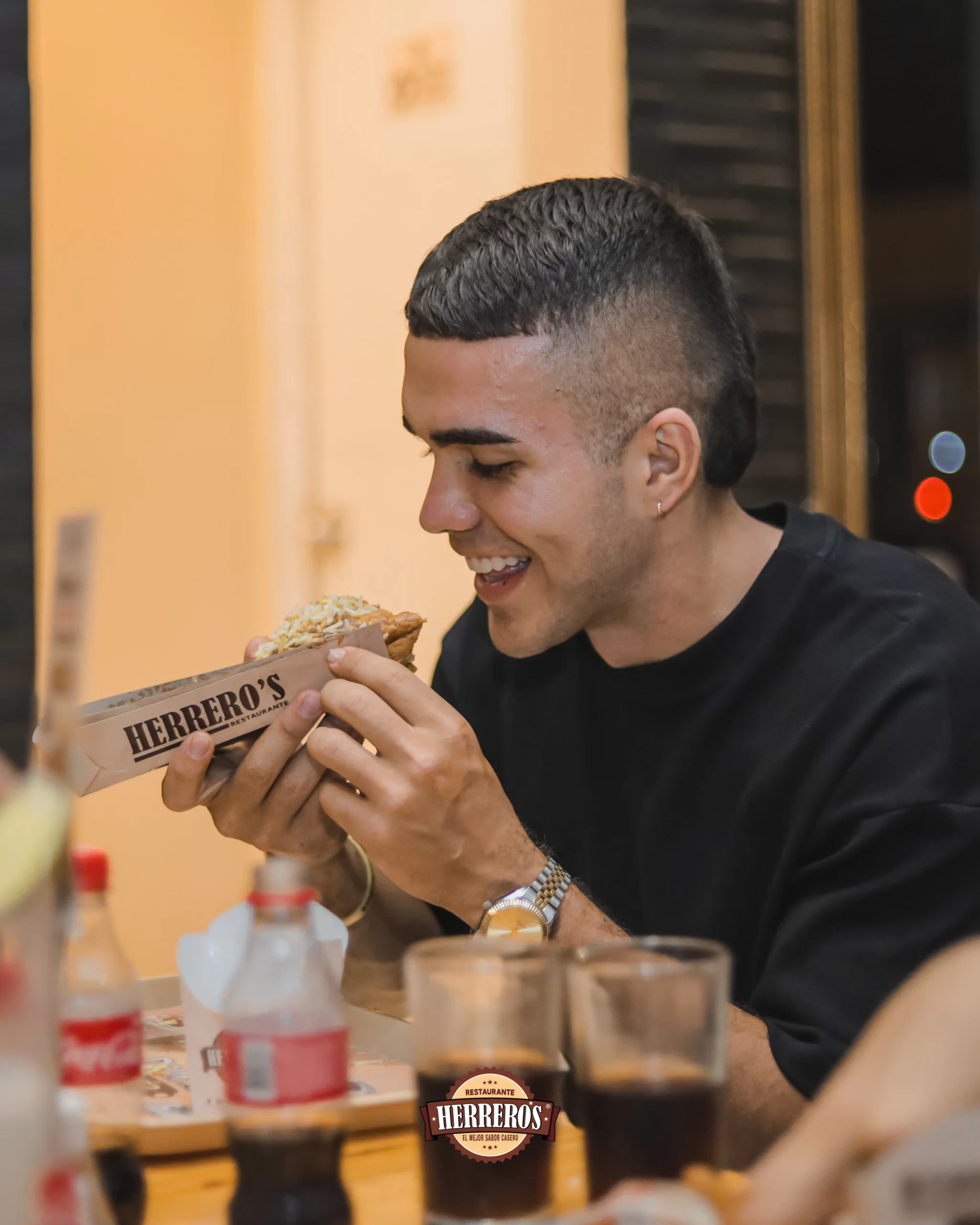 Hombre Joven mirando un perro caliente preparado por el restaurante Herreros.